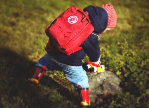 Mochila kanken para niños roja en la espalda de un crío que juega sobre una roca